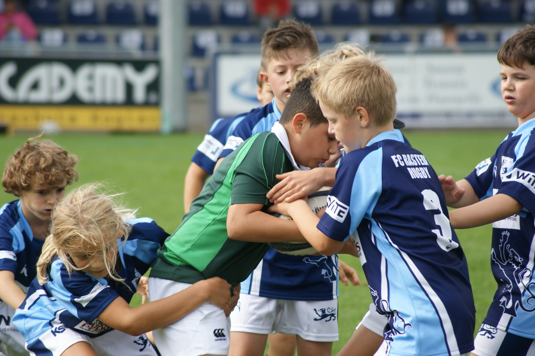 Kinder beim Rugbytraining mit Ball in blauen und grünen Trikots